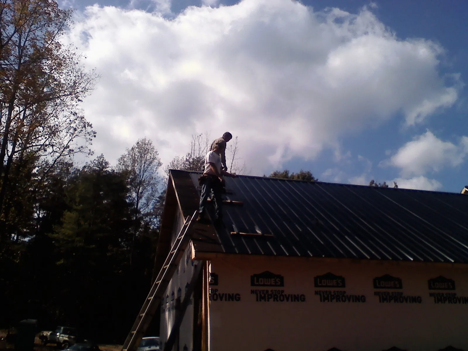 Roofer fastening dark metal panels high against a cloudy sky, from a Roof Inspection job in Egg Harbor Township