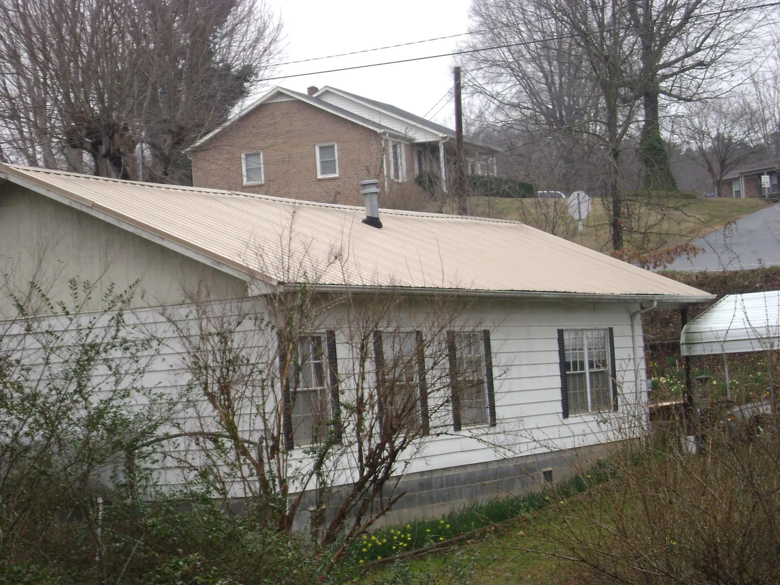 Tan metal roof on a white sided house set into a hillside — Commercial Roofing by Roofing Brothers in Egg Harbor Township